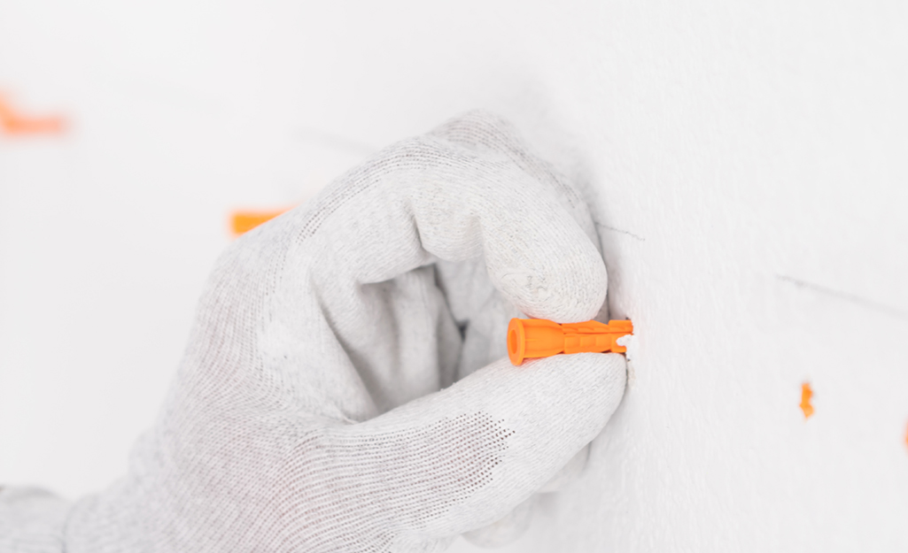 A person inserts an anchor into a pilot hole. A person inserts an anchor into a pilot hole.