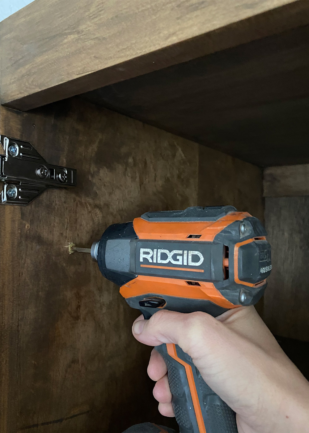 close up shot of a hand drilling a hole on the side of a wooden board with a hand drill