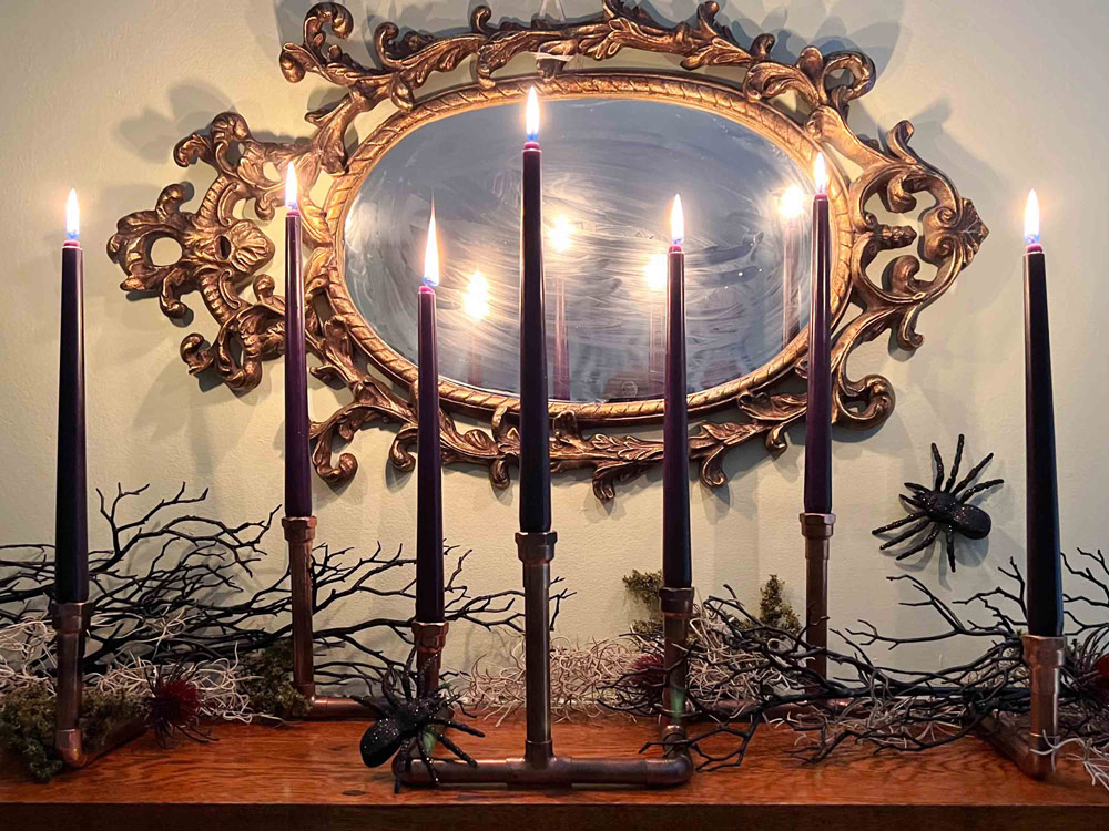 Creepy candles are displayed on a tabletop in front of a scary decorated mirror, candles are lit.