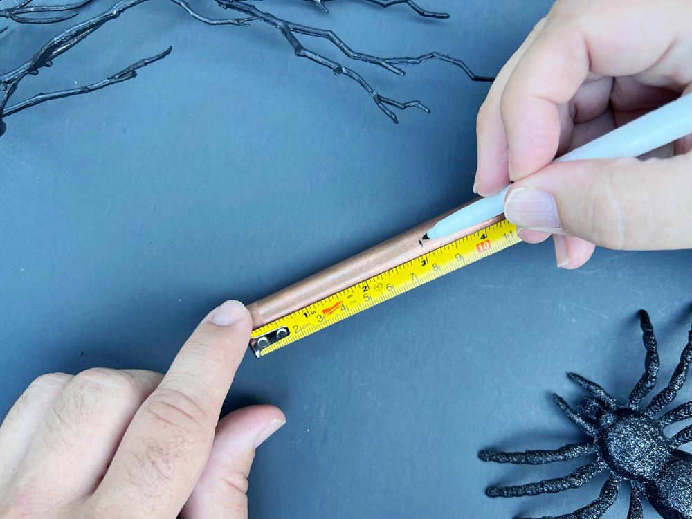 A hand measuring a copper pipe before cutting it.