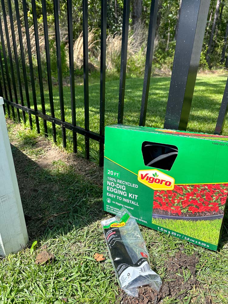 Vigoro No Dig Edging Kit in box sitting against black fence on green grass ground.