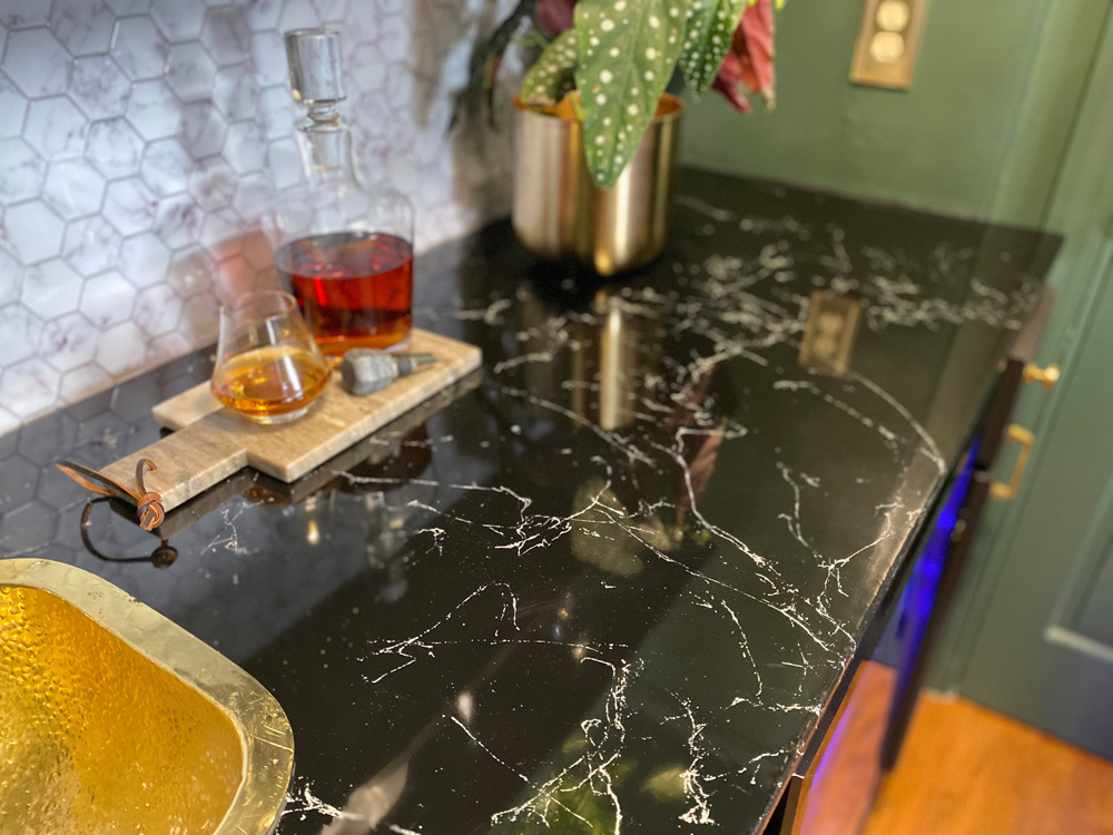 Countertop featuring cutting board with drinking glass, glass vessel and potted plant.