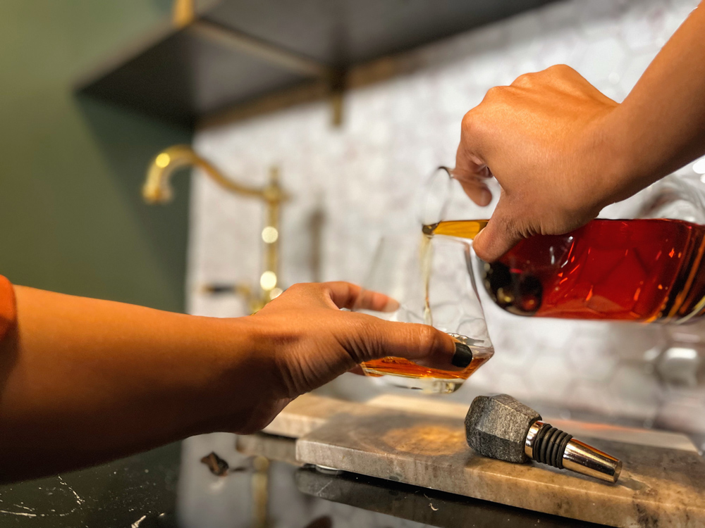 A woman’s hands pouring beverage into drinking glass.