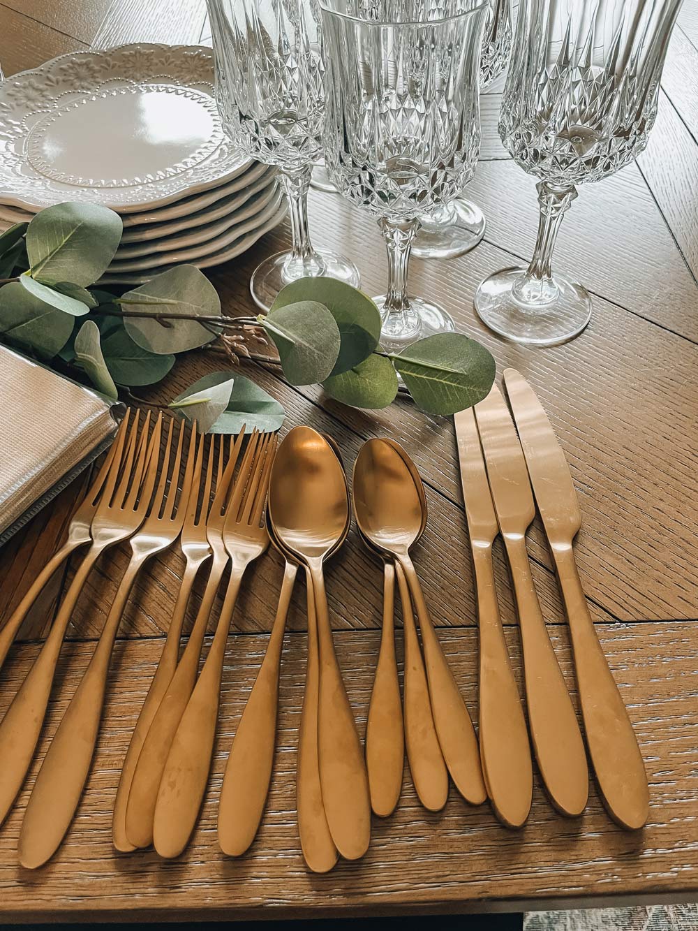Gold hardware utensils with glasses on a dining room table.