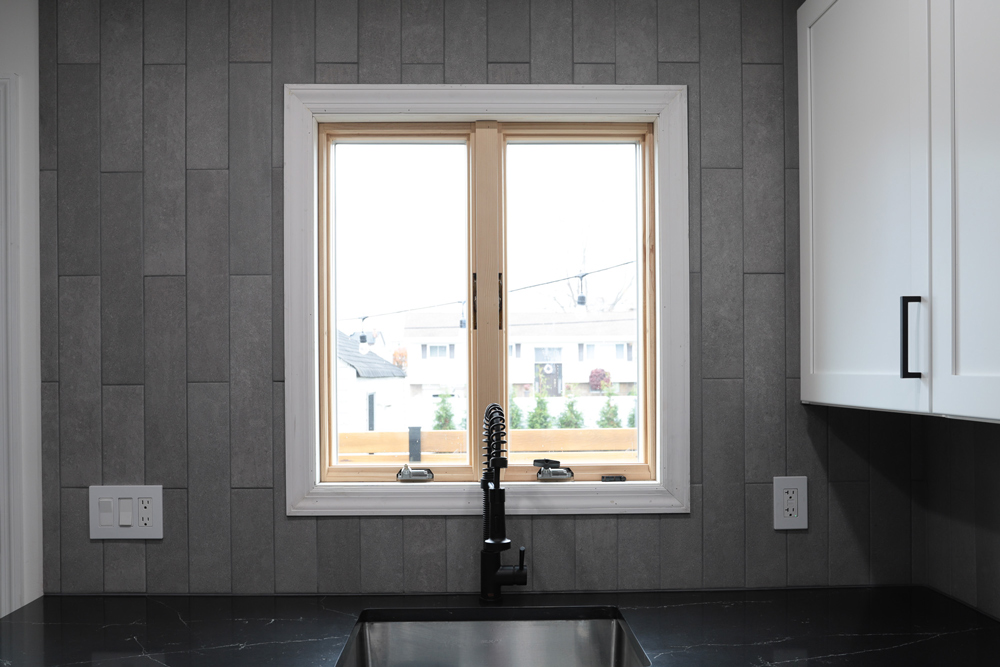 Front view of a kitchen window with gray tiling, and black marble countertop.