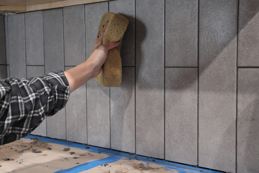 A person using a wet sponge to wipe away excess grout from tiles.