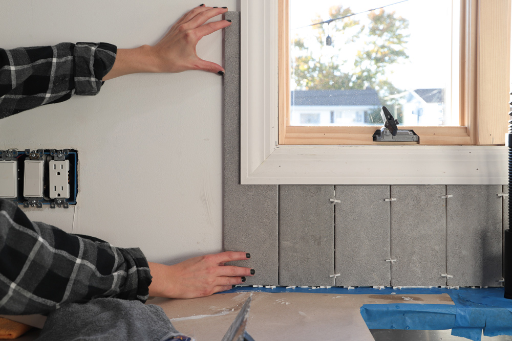 A person fitting a piece of tile on the side of a window.