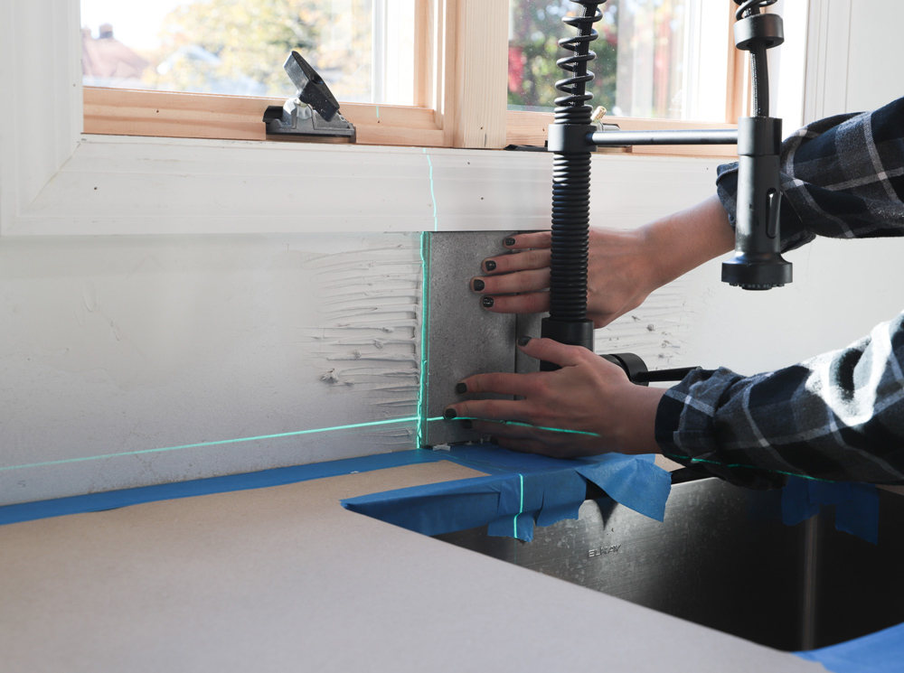 A person placing tiles to the adhesive underneath a window.