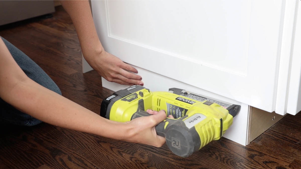 Person using a Ryobi tool to install a filler board to the base of the cabinet.