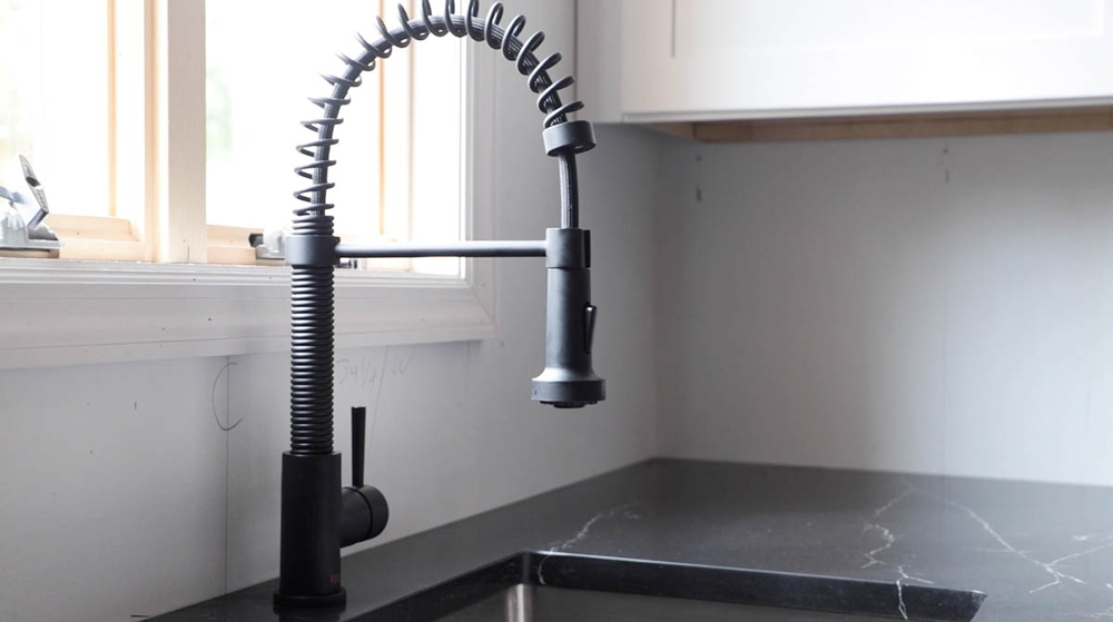 Sink faucet installed into counter with black marble countertops.