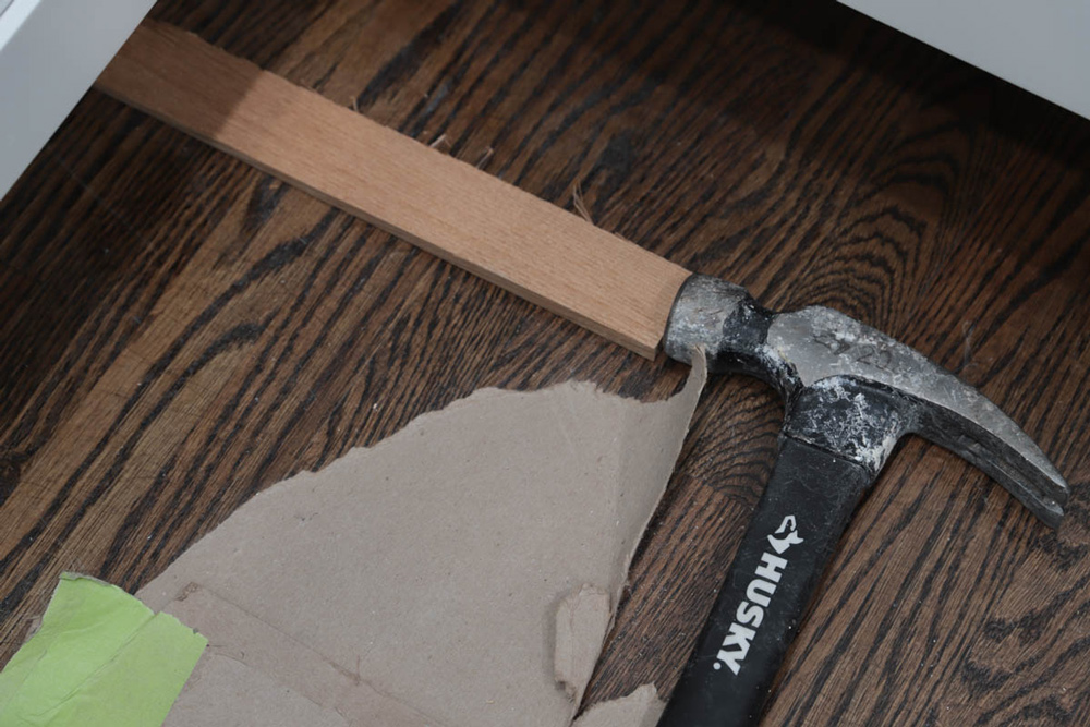 A Husky hammer laid on the floor against a wood slat.