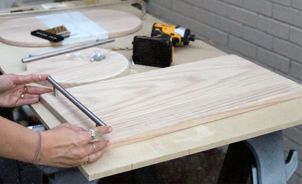 A person adding handles to a cheeseboard design.