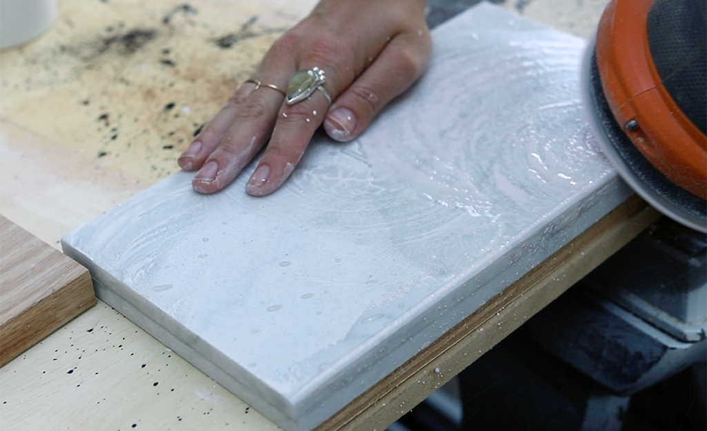 A person using a sander on a tile edge.