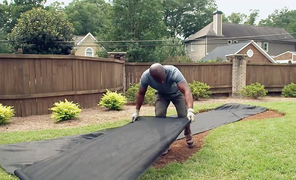 A person laying landscape fabric to create a putting green.