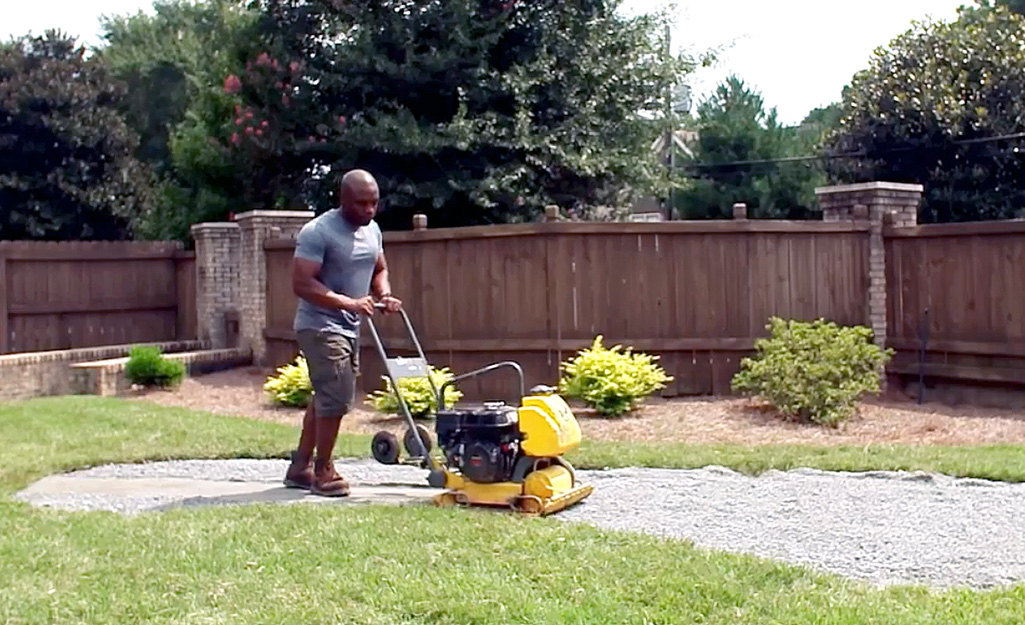 A person smoothing a base of crushed rock for a DIY putting green.