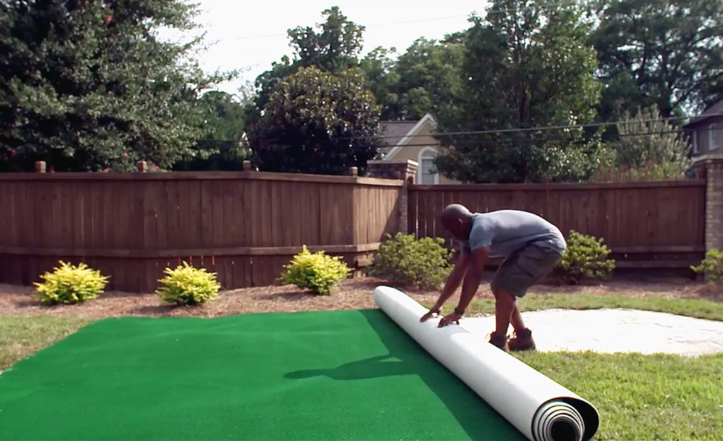 A person laying out synthetic turf for a putting green.
