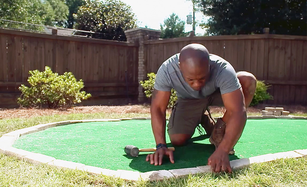 A person installing a paver stone border around a DIY putting green.