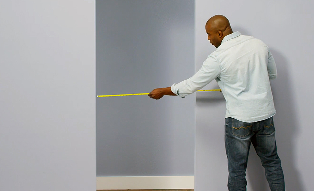 A man uses a tape measure on a doorway.