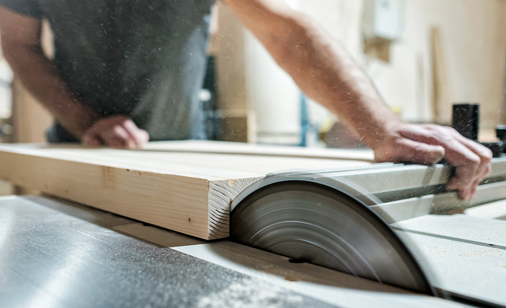 A worker trims wood board with a table saw.