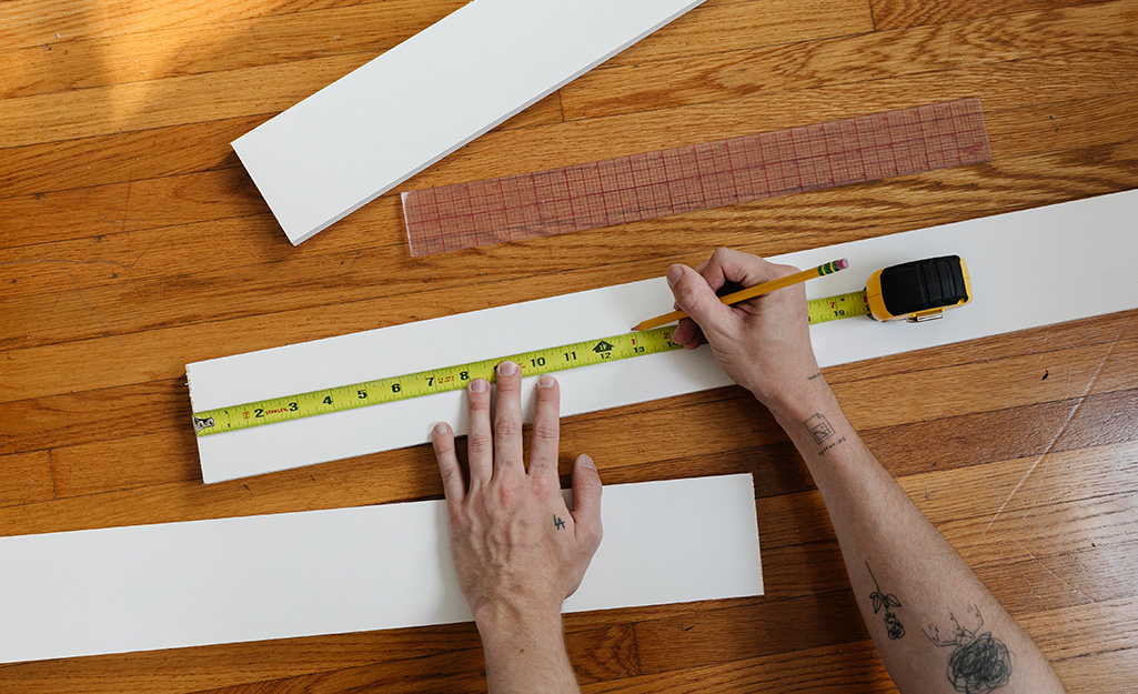 A person measuring a board to create boards and battens for an accent wall.