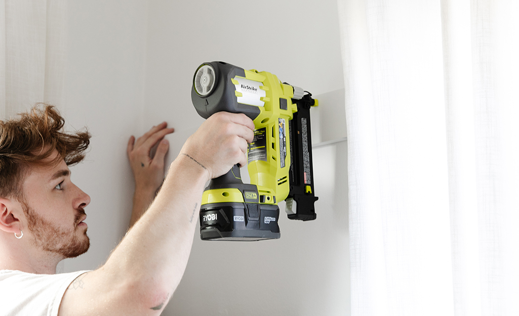 A person using a nailer to attach boards to an accent wall.