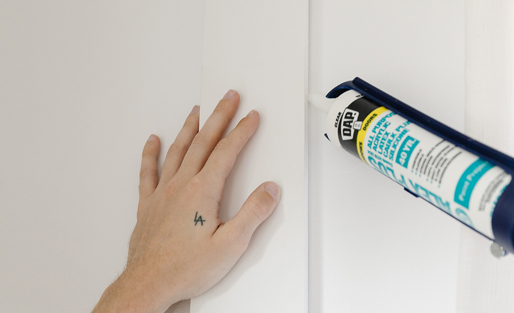 A person caulking the edges of a wall board.