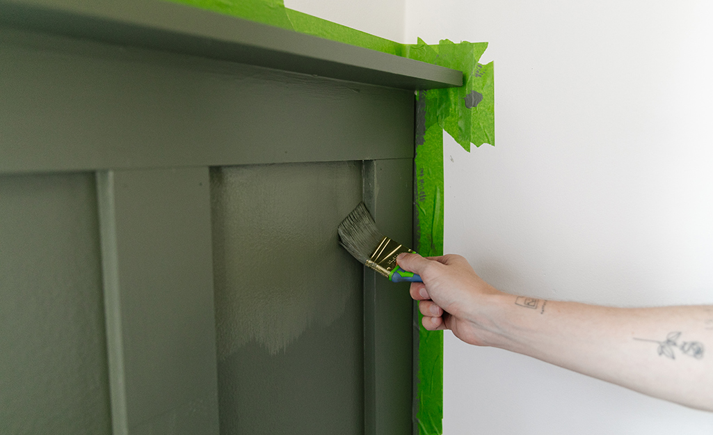A person painting an accent wall with green paint.