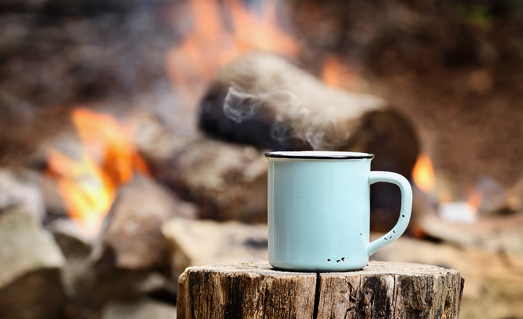 Blue coffee cup sitting on a tree stump in front of a fire.