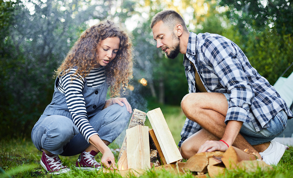 Couple trying to start campfire outdoors.