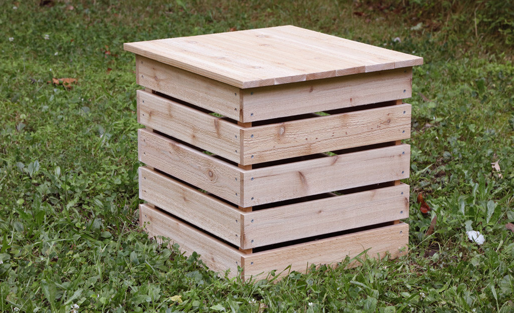 A wood DIY compost bin sitting in the grass.