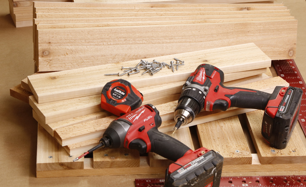 Power tools, screws and a tape measure placed on wood boards.