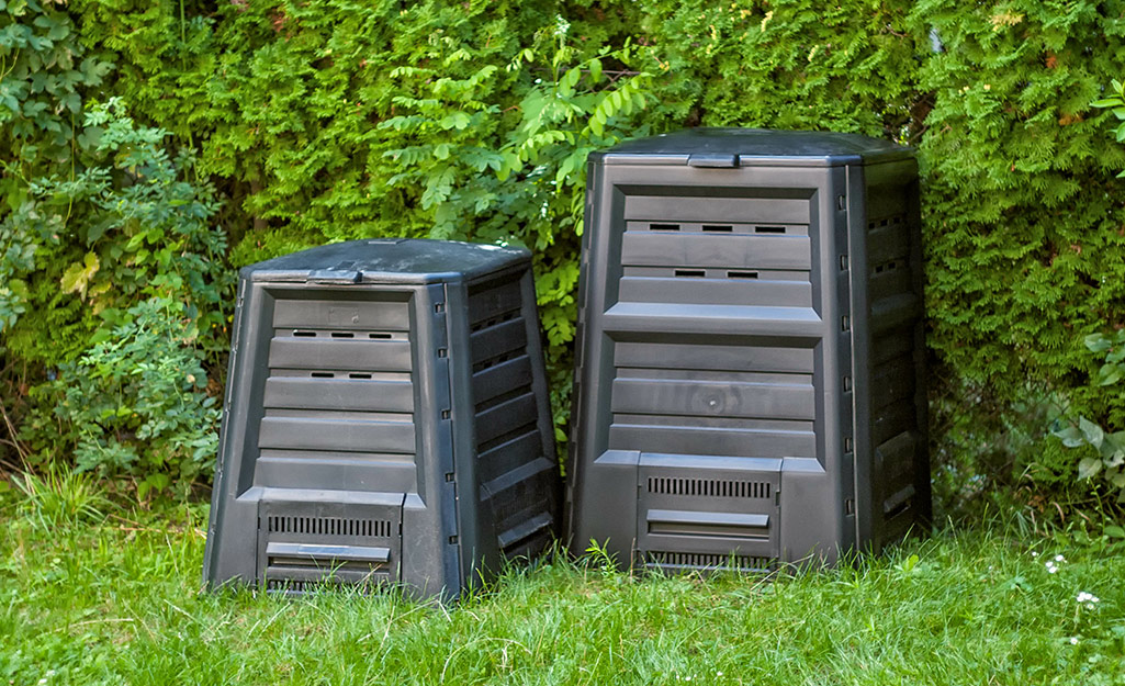 Two plastic bins placed in front of a hedge.