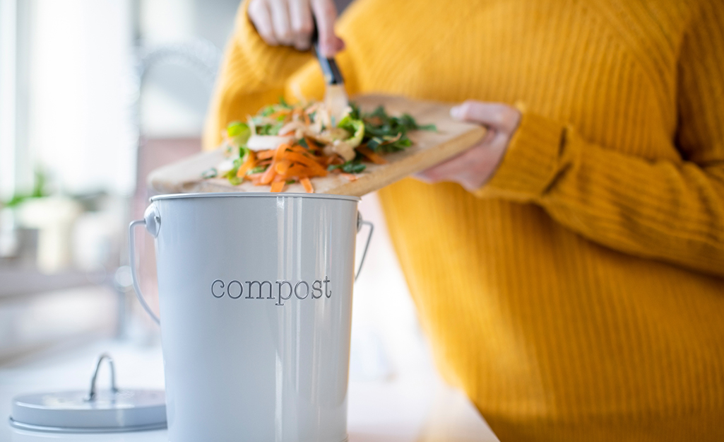 Someone putting table scraps into a kitchen compost bucket.