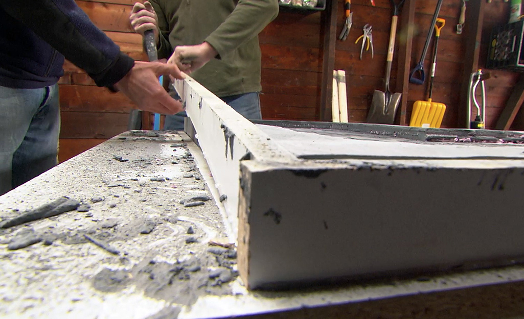 Two people removing a form to release the concrete countertop.