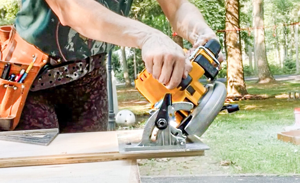 A person using a circular saw to cut boards.