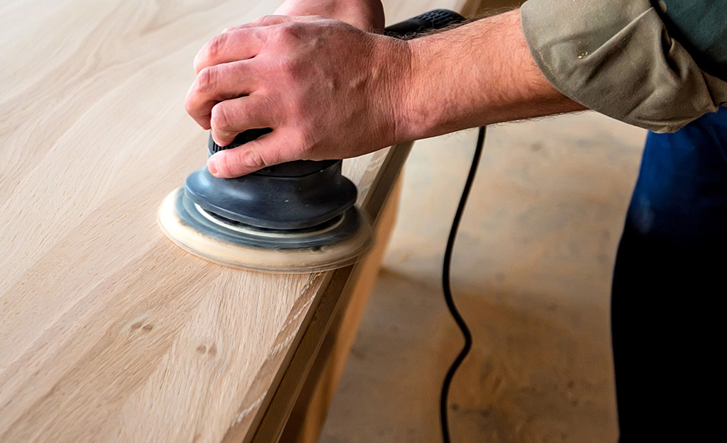 A person using a power sander to smooth boards.