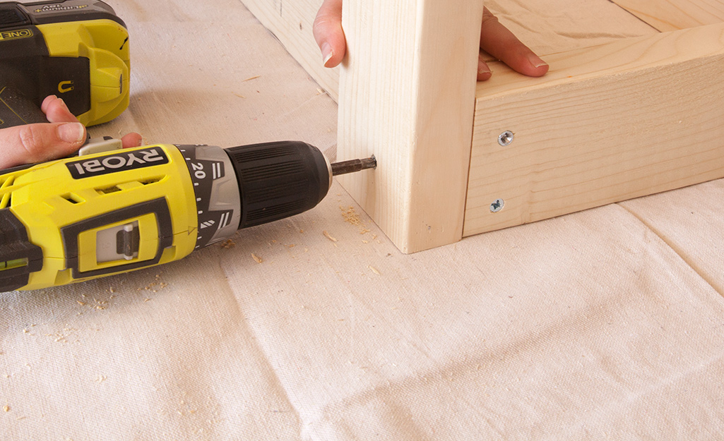 A person using a power drill to secure a corner board. A person using a power drill to secure a corner board.