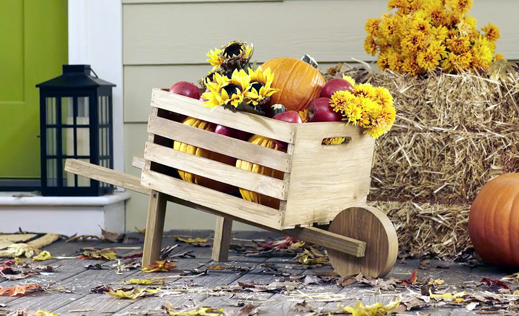 A decorative wheelbarrow filled with fall decor sitting on a porch.