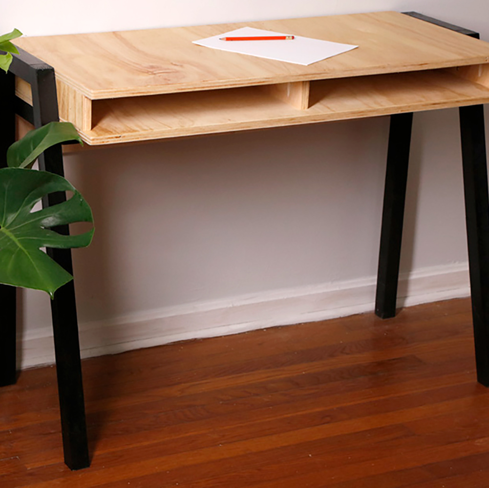 A blank piece of paper and an orange pencil rest on the wooden top of a DIY desk that has black legs. A blank piece of paper and an orange pencil rest on the wooden top of a DIY desk that has black legs.