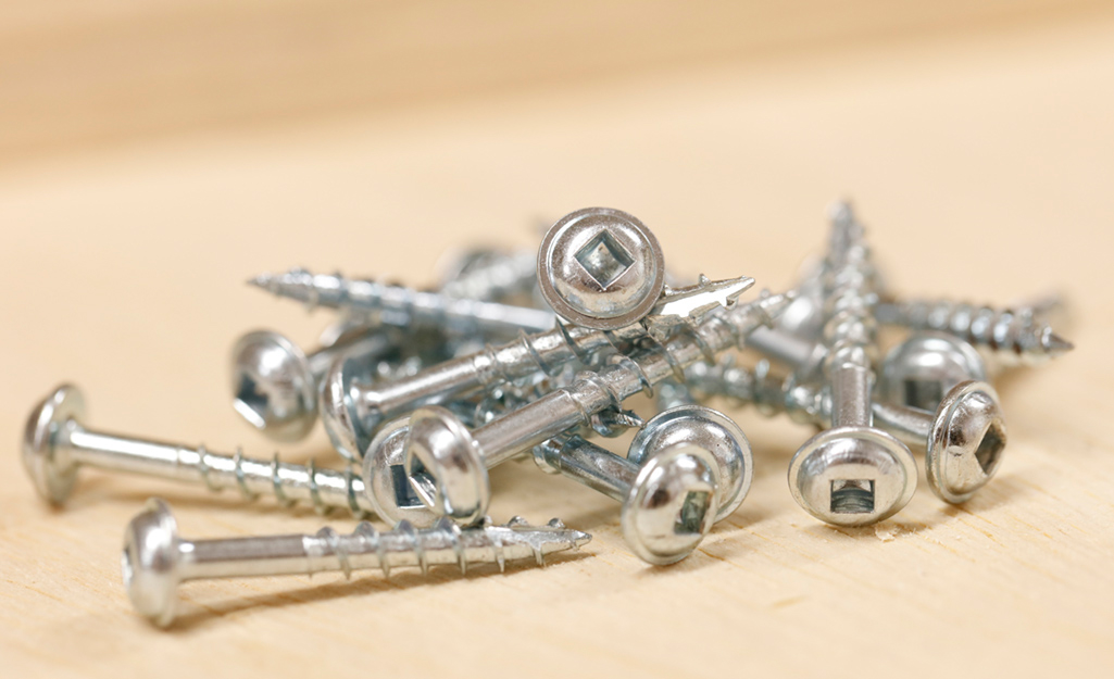 A small pile of screws lays on top of a piece of wood. A small pile of screws lays on top of a piece of wood.