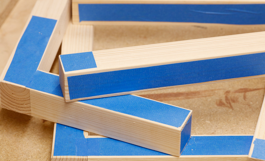 Blue painters tape covers some of the wooden pieces of a DIY desk project before they are assembled. Blue painters tape covers some of the wooden pieces of a DIY desk project before they are assembled.