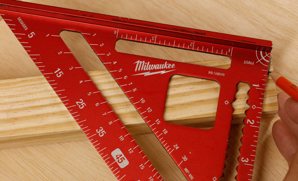 A person uses a pencil and a red speed square to mark measurements on a piece of wood. A person uses a pencil and a red speed square to mark measurements on a piece of wood.