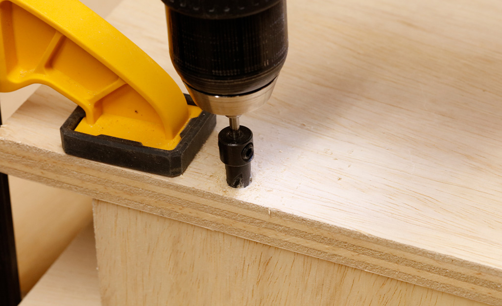 Countersink holes are drilled into plywood piece that serves as the top of a DIY desk. Countersink holes are drilled into plywood piece that serves as the top of a DIY desk.