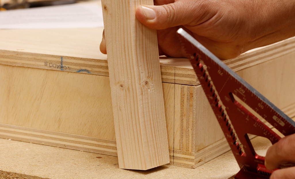 A person begins attaching legs to the wooden box of a DIY desk, which has been placed upside down. A person begins attaching legs to the wooden box of a DIY desk, which has been placed upside down.