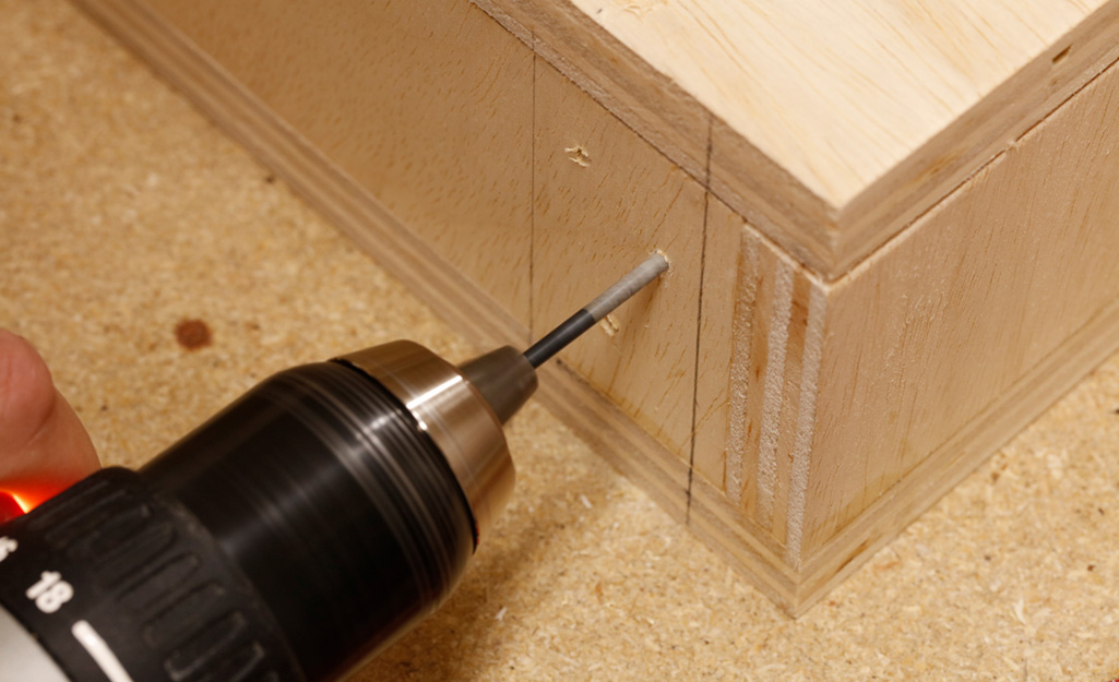 A drill is used to make freehand pocket holes near the corner of the wooden box of a DIY desk. A drill is used to make freehand pocket holes near the corner of the wooden box of a DIY desk.