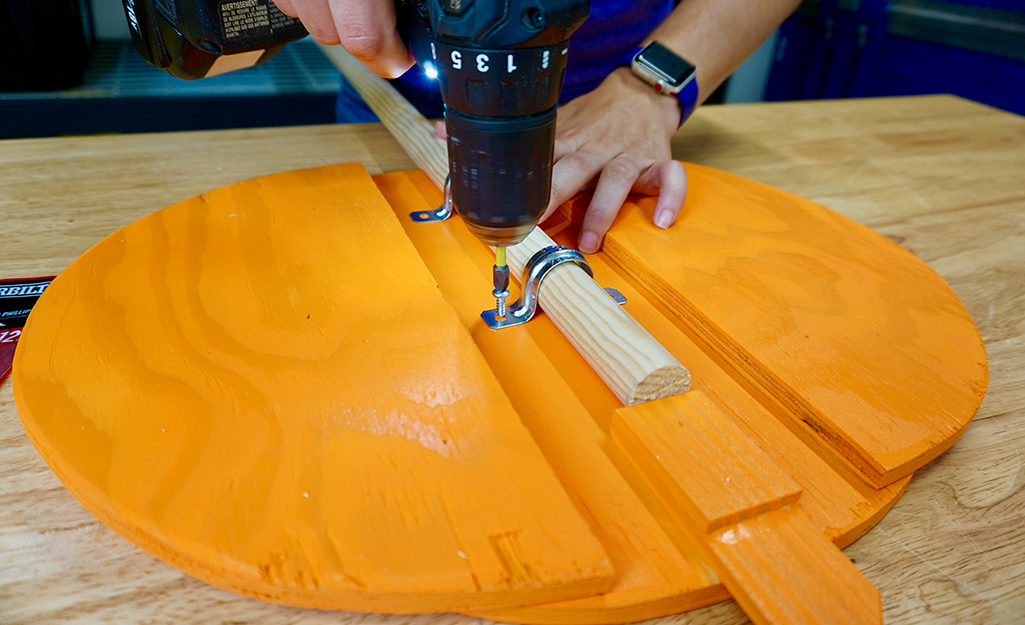 A person attaching a dowel to the wood pumpkin. A person attaching a dowel to the wood pumpkin.