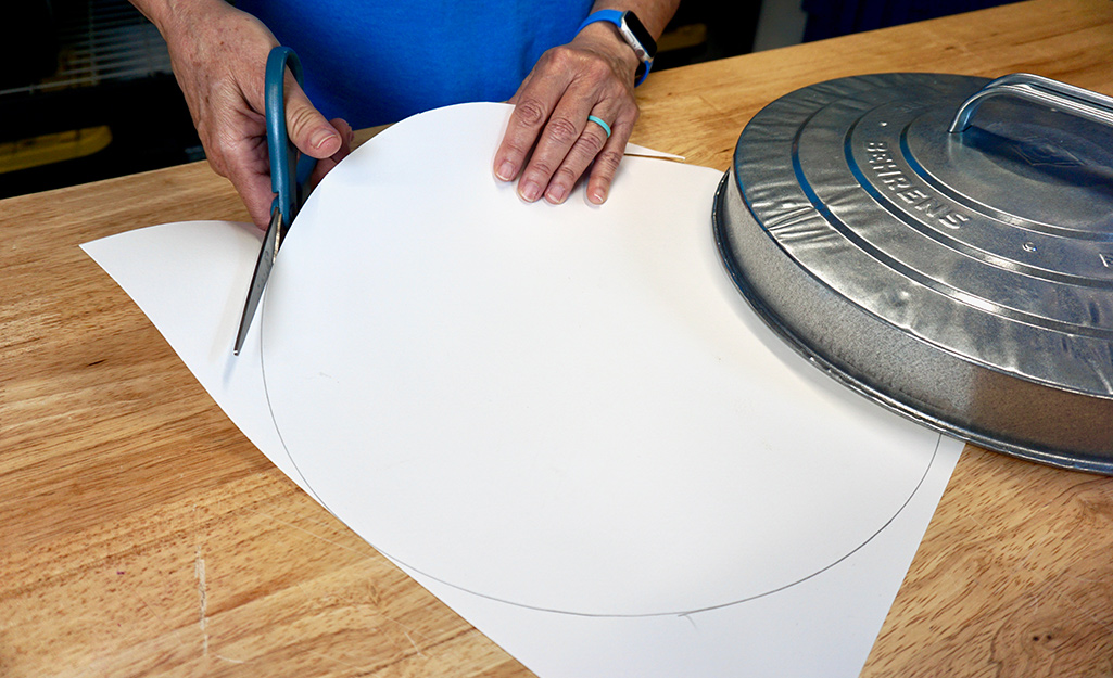 A person cutting out a round template to create a pumpkin. A person cutting out a round template to create a pumpkin.