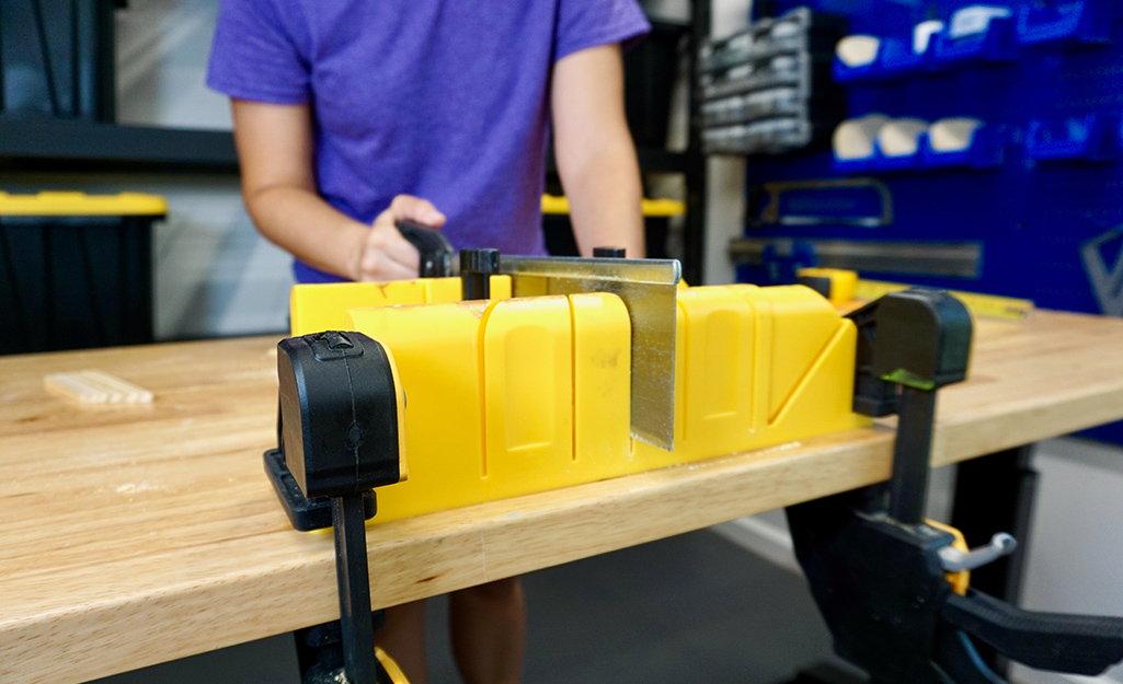 A person using a miter box and hand saw. A person using a miter box and hand saw.