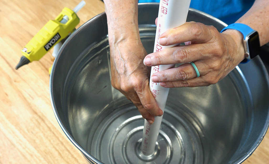 A person setting a PVC pipe into a bucket with hot glue. A person setting a PVC pipe into a bucket with hot glue.