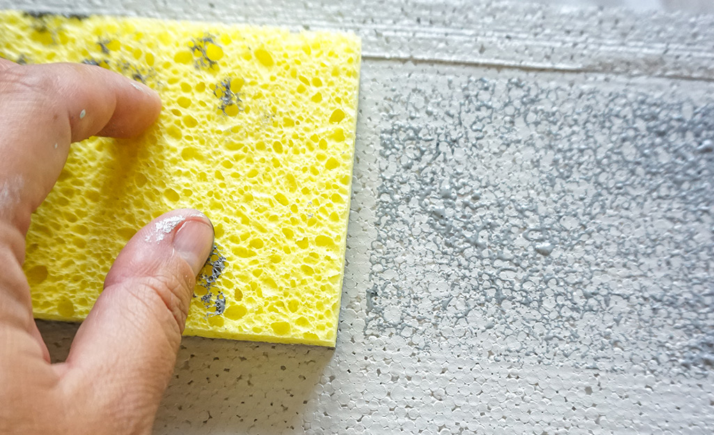 A person using a sponge to create a brick pattern on the foam.
